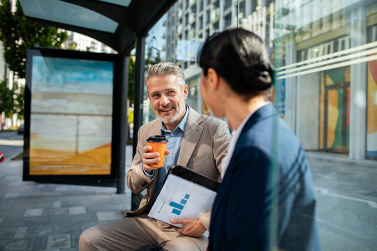 Business colleagues chatting with coffee at city bus stop