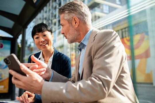 Two business colleagues discussing smartphone at city bus stop