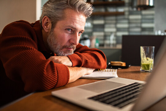 Tired middle-aged man at laptop in home kitchen