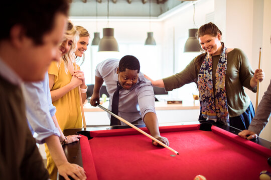 Diverse coworkers playing pool together in modern office break room