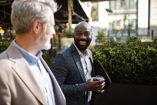 Smiling businessmen having coffee conversation on city sidewalk