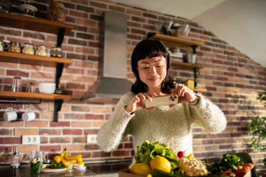 Smiling woman photographing fresh vegetables in home kitchen