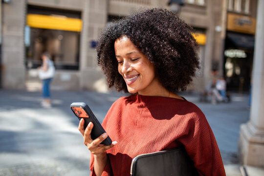 Smiling young woman using smartphone on city street
