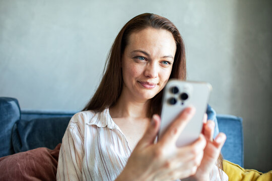 Smiling woman using smartphone on sofa at home