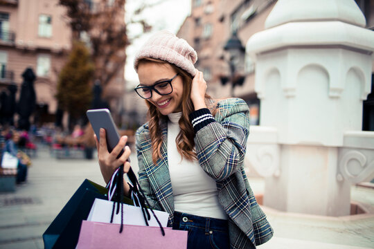 Smiling young woman using smartphone while shopping on city street