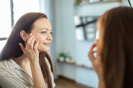 Smiling woman touching face at home mirror