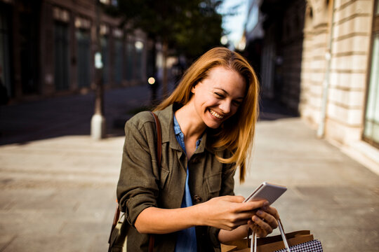 Smiling woman using smartphone while shopping on city street