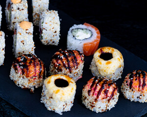 Single Baked Sushi Roll in Sharp Focus with Assorted Maki on Black Slate Plate, Japanese Restaurant Cuisine, Vertical Close Up Food Photography with Selective Focus © vitorust