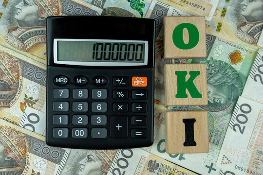 calculator displaying financial numbers on zloty banknotes with wooden blocks spelling OKI for new personal investment account tax law reform