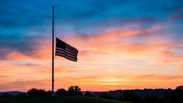 American flag at half mast during a vibrant sunset over rolling hills