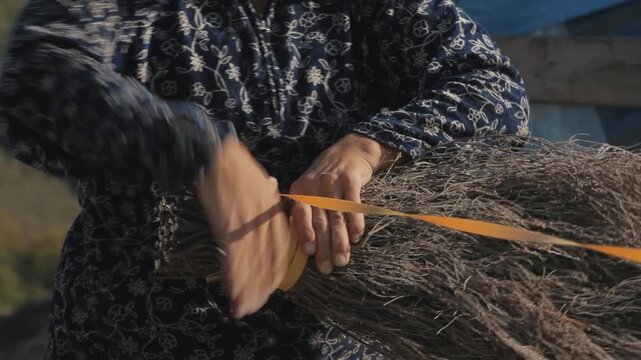 Close-up of artisan hands tightly binding dried branches to make a traditional handmade broom.