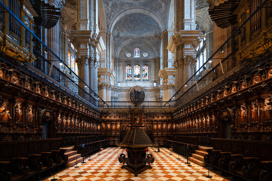 Symmetrical, wide perspective of the stunning choir stalls (siller&iacute;a del coro) and organ inside Malaga Cathedral, Spain, showcasing detailed dark wood carving.