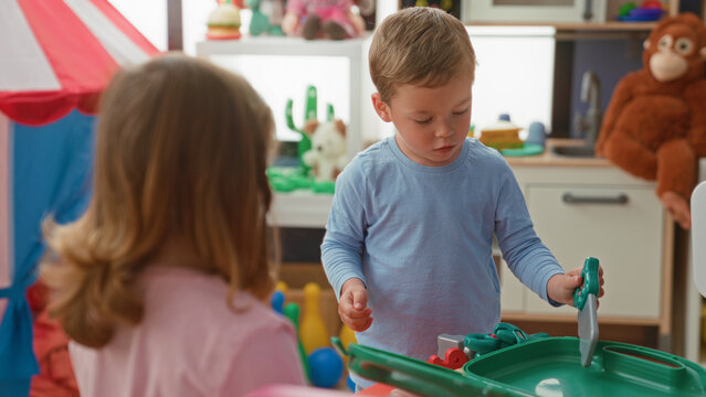 Boy holding a toy screwdriver, turning it with his hand in a building playroom among colorful toys while a girl watches nearby; concentration.