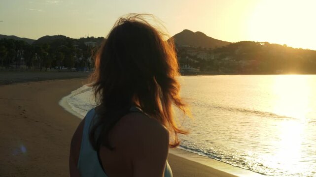 Woman embracing serenity, standing alone on a sun-kissed beach at sunset, gazing out at the calm sea with a sense of peaceful introspection and personal growth.