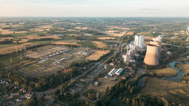 Industrial power plant with cooling towers surrounded by green fields and a canal under a clear blue sky, captured at sunset &mdash; symbol of modern energy and landscape harmony.
