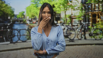 Fototapeta premium Thai woman touching her cheek with hand in a street canal scene wearing a blue blouse and bracelet; thoughtful.