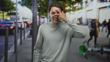 Fototapeta premium Man covering right eye with hand while smiling beside a fallen green electric scooter on a busy street sidewalk; playful curiosity.