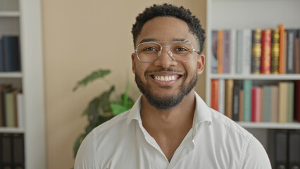 Man wearing glasses smiling directly at camera in a study building with bookshelves and plant visible  confidence success. © Krakenimages.com