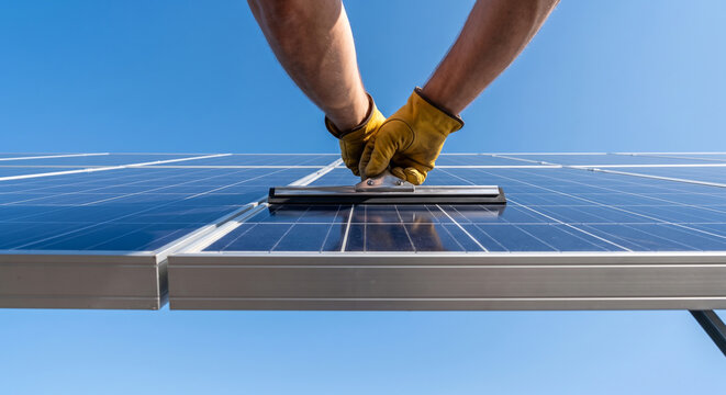Cleaning solar panel with squeegee on sunny day blue sky clean energy sustainability renewable power source maintenance.