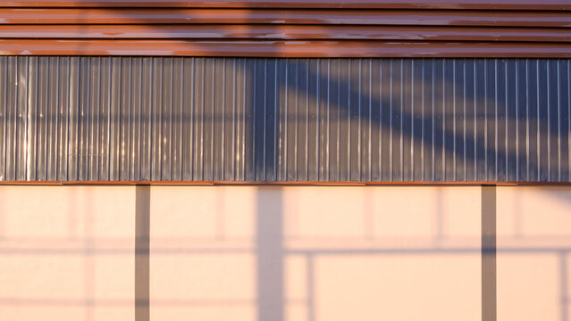 Corrugated metal wall of modern warehouse with geometric shadows and warm sunlight, industrial building background texture