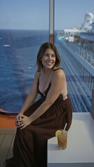 Fototapeta premium Woman smiling and sitting showing cleavage on cruise ship terrace with ocean view and drink nearby; relaxed serenity.