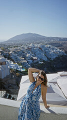Fototapeta premium Woman raising arm with sunglasses on a white building terrace, leaning on a wall and smiling at the view; vacation serenity.