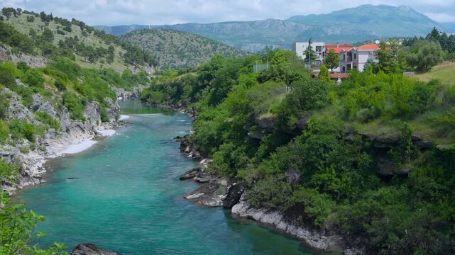 Turquoise Moraca river flowing through a green rocky canyon with hills and houses in Podgorica, capital of Montenegro, scenic summer travel destination, wild landscape.
