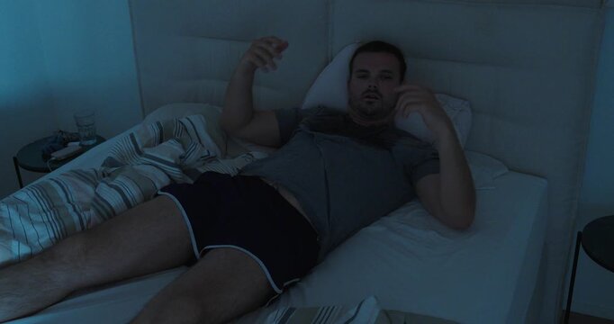 Man lying awake in bed sweating during a hot night, representing heatwave discomfort, insomnia and summer sleep problems.