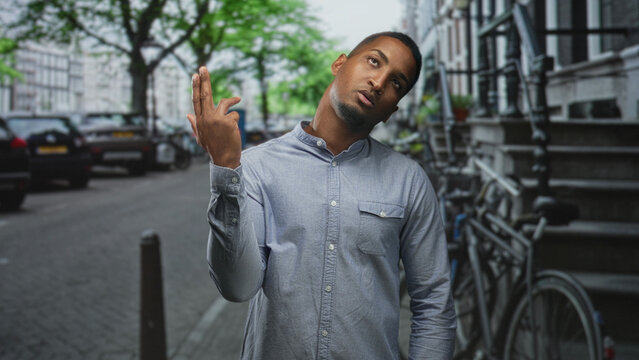 Black man points finger to temple and shows middle finger on a street lined with bicycles and parked cars; defiance urban attitude.
