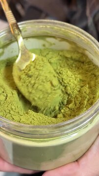 Matcha powder spooning, green tea extract being scooped from container into metal pitcher, preparation of healthy traditional Japanese beverage in professional kitchen