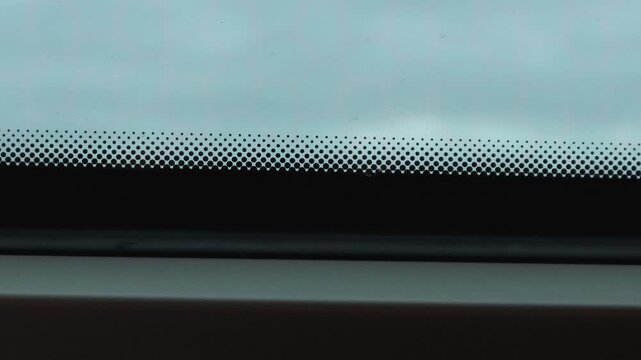 View through a train window with passing power poles, cloudy sky, and blurred movement outside.

