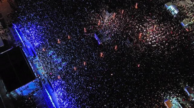 Aerial top view of crowd at night music concert. People gathered at festival outdoor stage with lights and screens, 4k