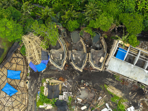 Aerial view of a construction site featuring bamboo structures, pools, and blue tarps surrounded by lush tropical greenery in Sidemen, Bali, Indonesia.
