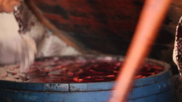 A person uses a wooden stick to stir a barrel of fermenting purple carrots. An authentic look at the preparation process of traditional Turkish turnip juice (şalgam).