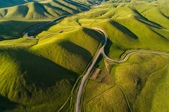 Aerial view of winding roads cutting through lush green rolling hills under bright sunlight in Kern County, California, United States.