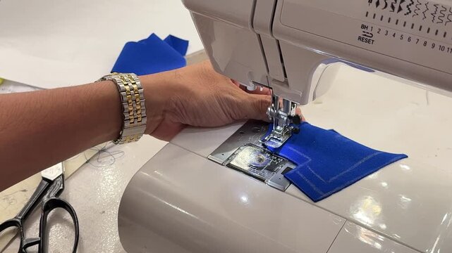 Close-up of tailor hands sewing blue fabric on a professional sewing machine