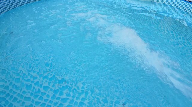Sunlit backyard pool surface with concentrated white foam band and bubbling return flow spreading across turquoise water beside tiled edge in calm residential setting