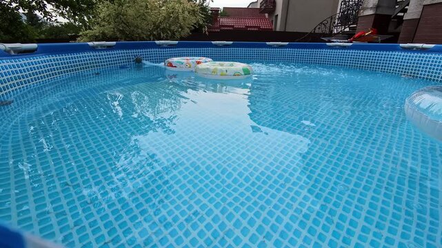 Backyard above ground pool with floating inflatable rings and gentle ripples viewed from low waterline