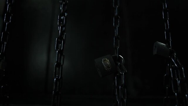 Close-up of heavy metal chains and padlocks hanging in the dark. Ideal for security or mystery themes.