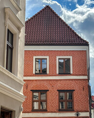 Obraz premium Old brick building – Low-angle view of a restored Gothic red facade with arched window surrounds, wooden cross-paned windows and a steep tiled gable roof in the historic old town of Torun, Poland.