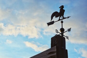Silhouette of a Traditional Rooster Weathervane Against a Cloudy Blue Sky © Nick