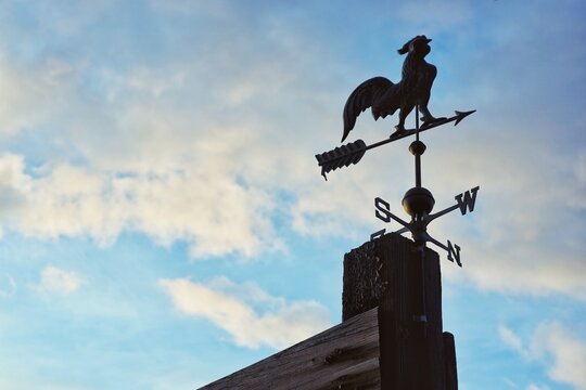 Silhouette of a Traditional Rooster Weathervane Against a Cloudy Blue Sky