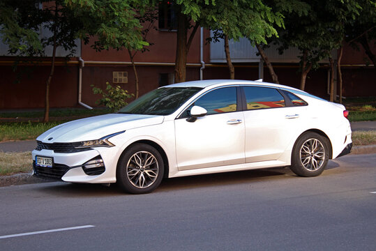 Vinnytsia, Ukraine; April 18, 2026. White KIA K5 2023 at the parking. Sleek, midsize sedan KIA K5 in city street. Korean business car KIA K5 parked on asphalt beside green trees in urban street settin