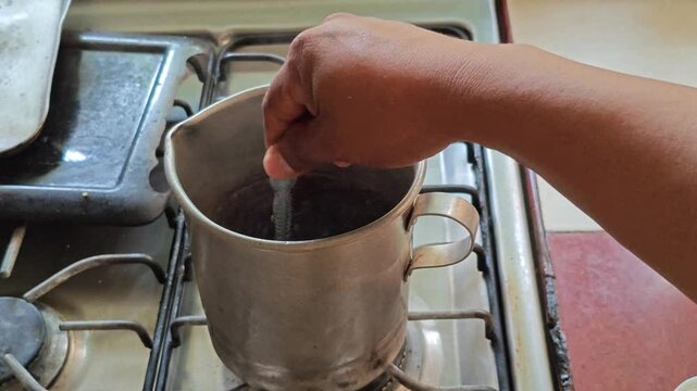 Hand stirring hot coffee with a spoon inside a pewter mug