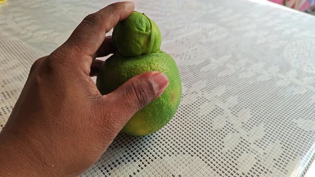 Hand turning a deformed organic orange on a wooden surface