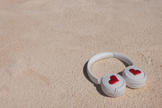 White headphones with hearts on the sandy beach.
