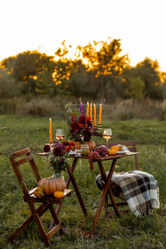 Cozy autumn table decoration for a thanksgiving party outdoors. Grapes, fig, rose wine, candles, pumpkins as decor. Elegant wedding fall arrangement, beautiful setting for a romantic proposal