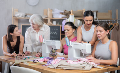 Obraz premium Busy women of different ages sewing and drawing with teacher at dressmaking class