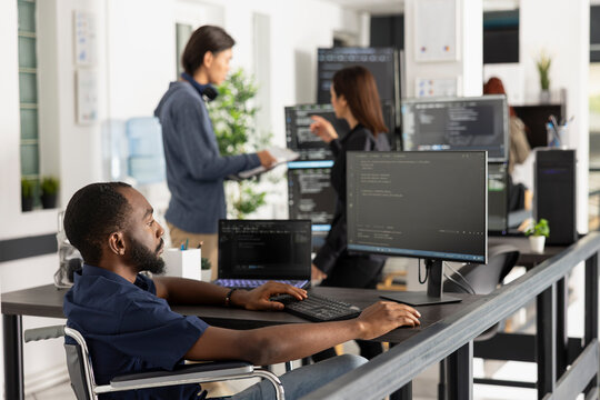 Focused programmer in a wheelchair works at a desktop computer in a modern startup office, representing accessibility, innovation and diversity in tech.