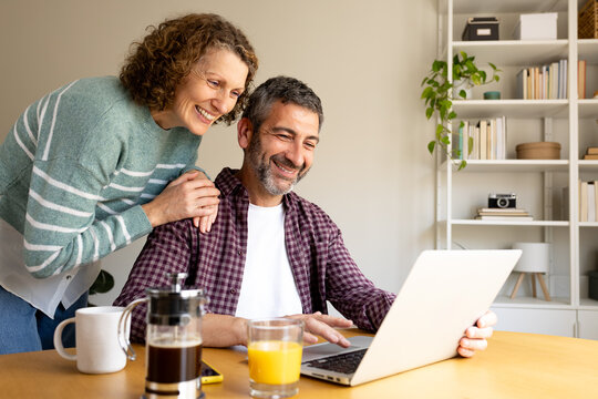 Mature couple smiling enjoying breakfast looking at laptop